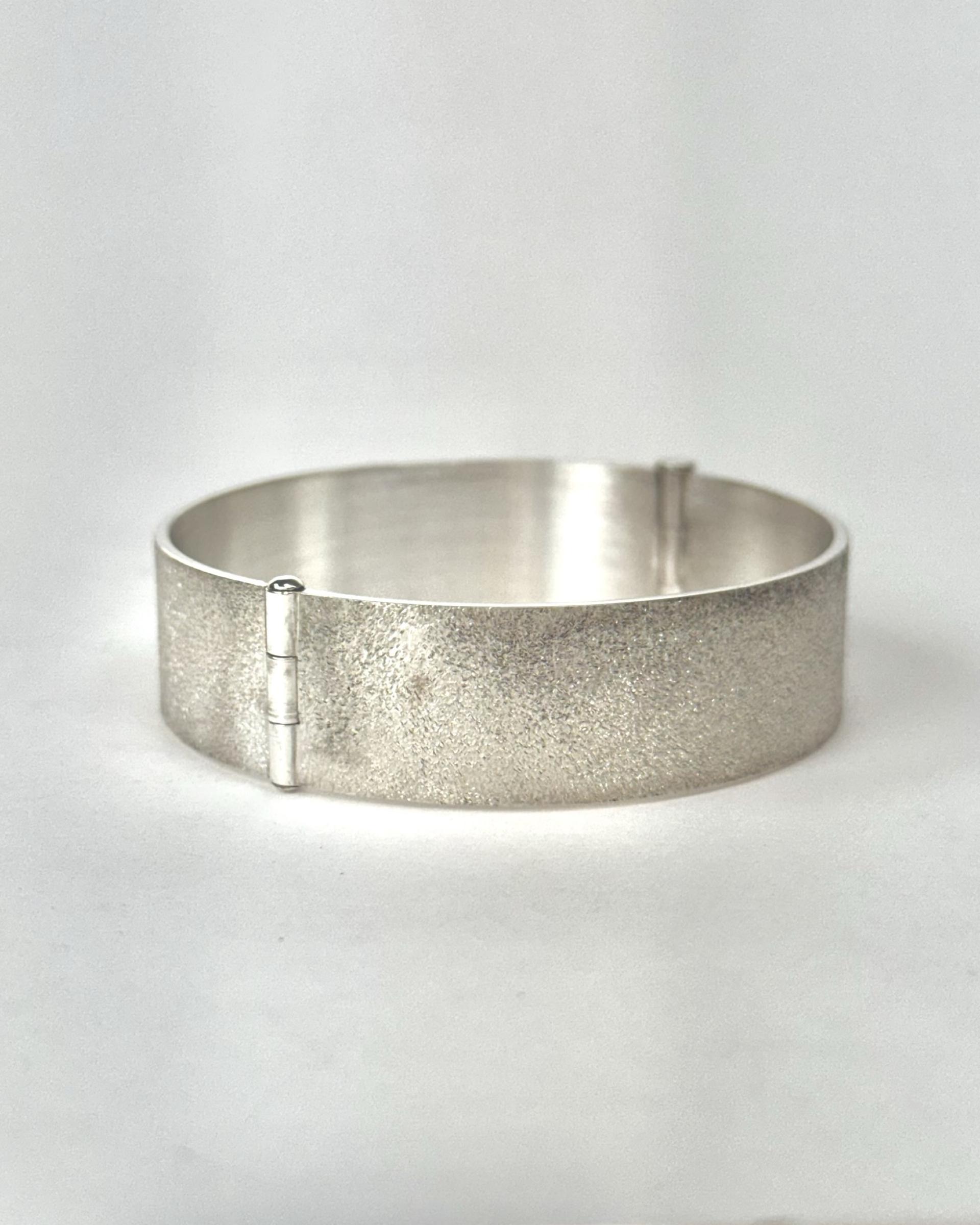 Hinged silver bracelet with grainy matte texture in its closed position.