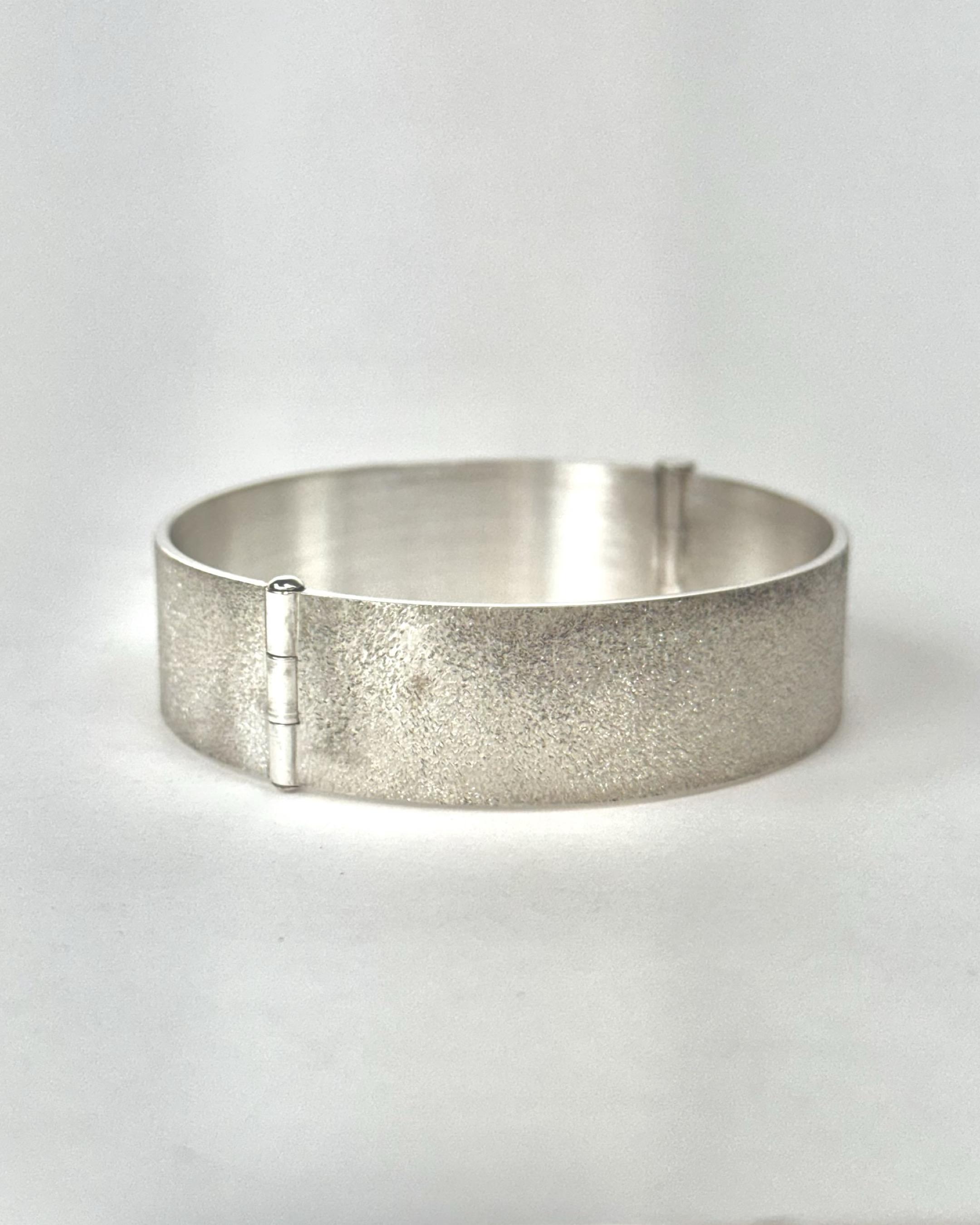 Hinged silver bracelet with grainy matte texture in its closed position.